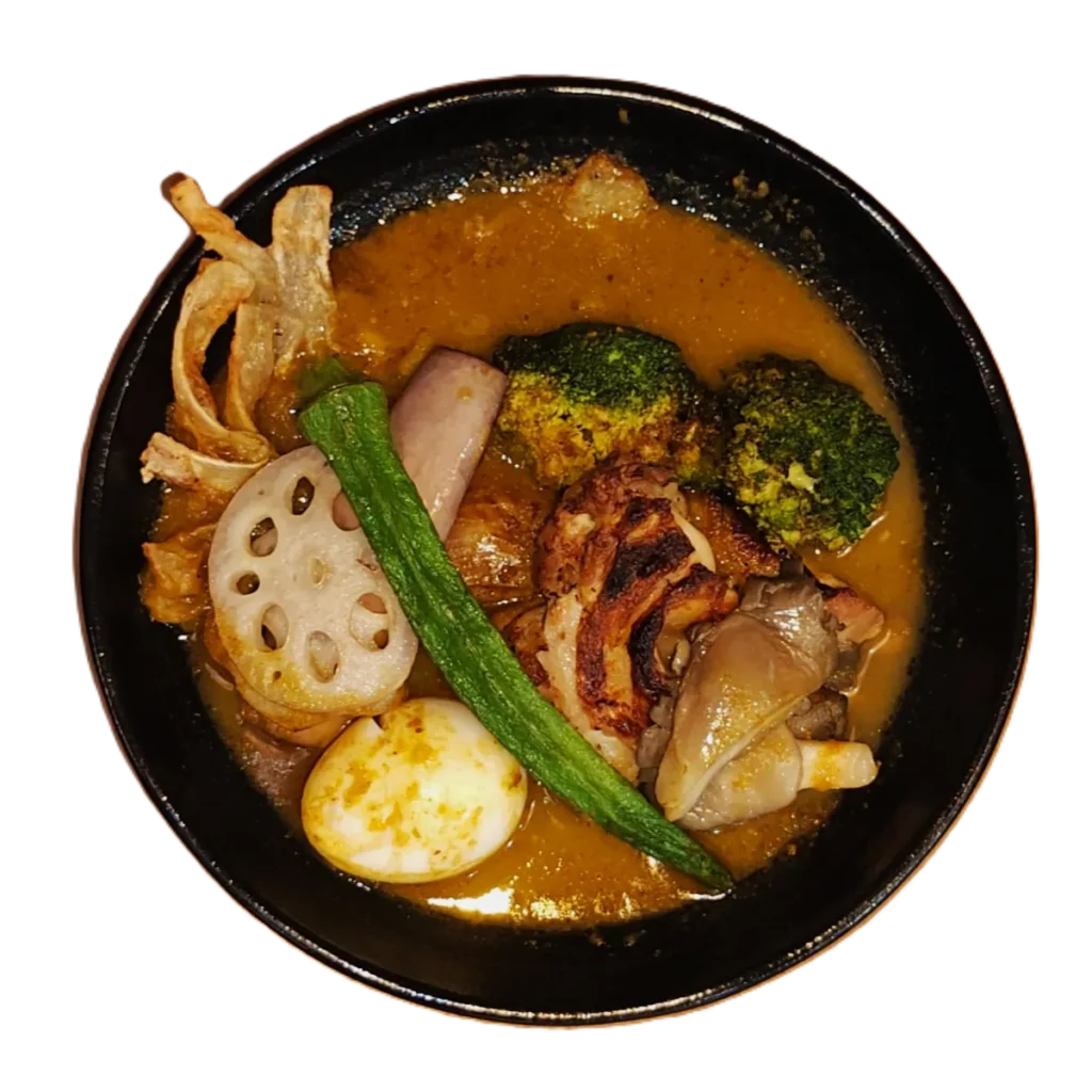 A bowl of curry featuring grilled meat, vegetables like broccoli and okra, sliced lotus root, and a boiled egg.