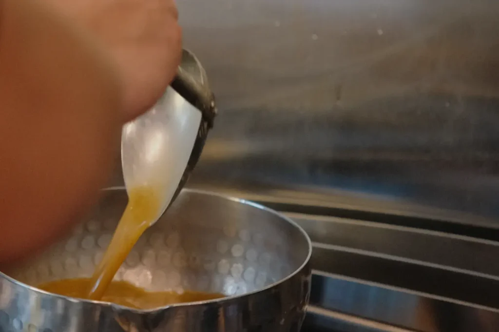 A person pouring liquid from a ladle into a metal bowl.