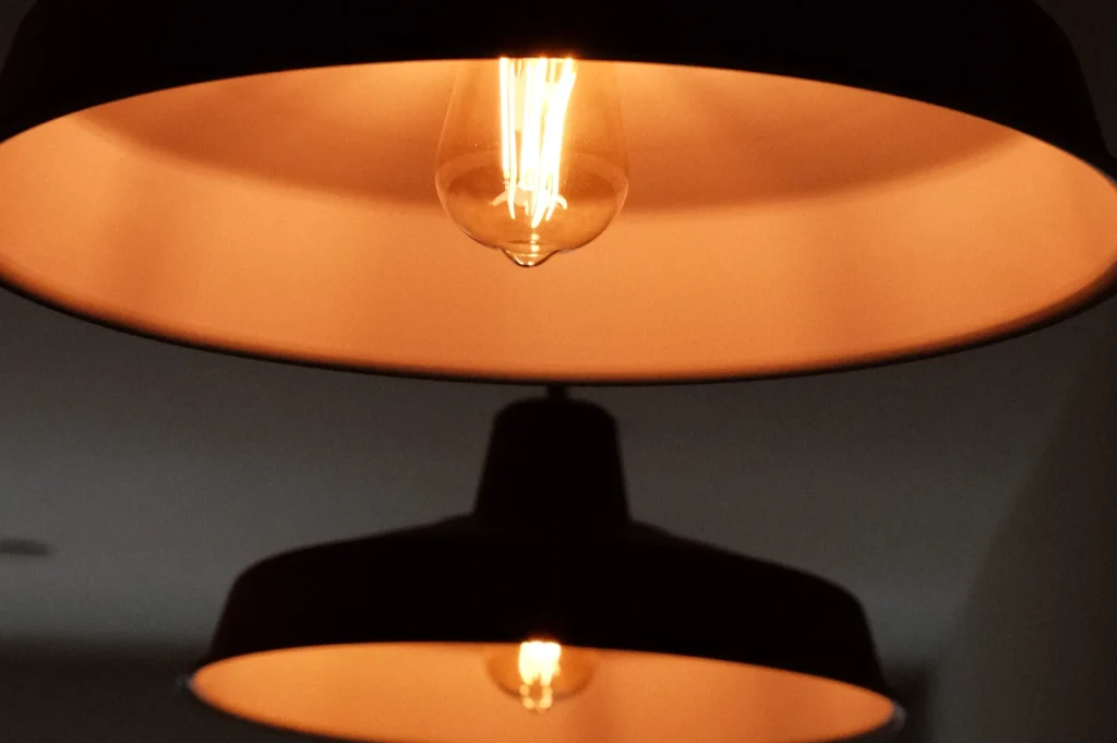 A close-up of hanging light fixtures with exposed bulbs, featuring a warm, amber glow against a neutral background.