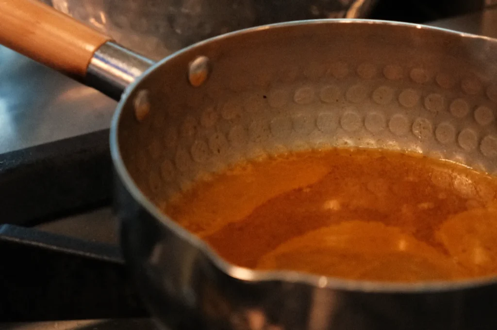A metal saucepan with a wooden handle, filled with a golden liquid, rests on a stove.