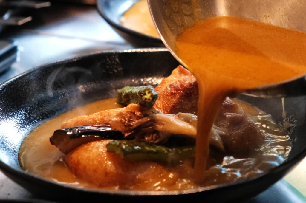 Soup curry being served, featuring a mix of vegetables and broth being poured into a bowl.