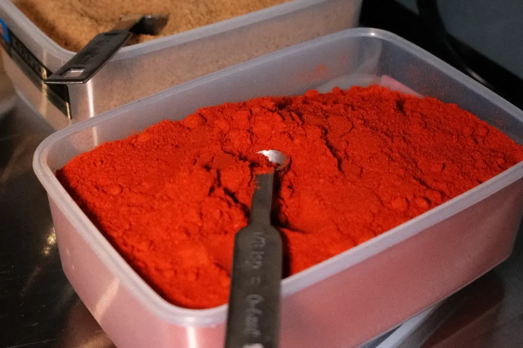 A container filled with red powder, likely spices, with a measuring spoon resting on top.