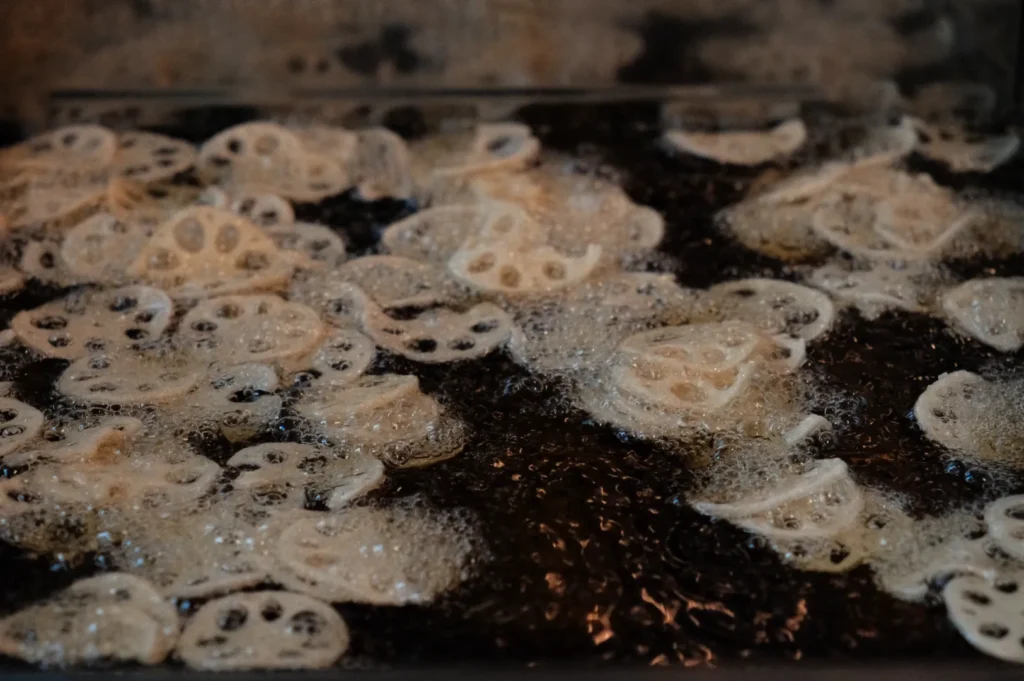 Lotus roots being deep-fried in oil, producing bubbles and a crispy texture.