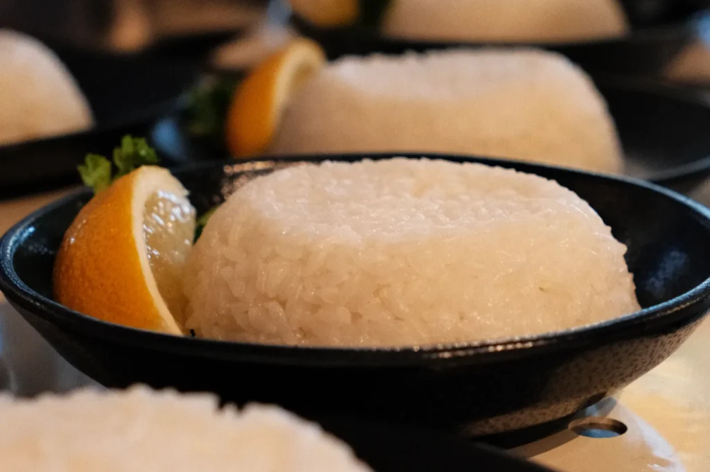 A close-up of a plate of white rice shaped into a mound, garnished with a lemon wedge and a sprig of parsley.