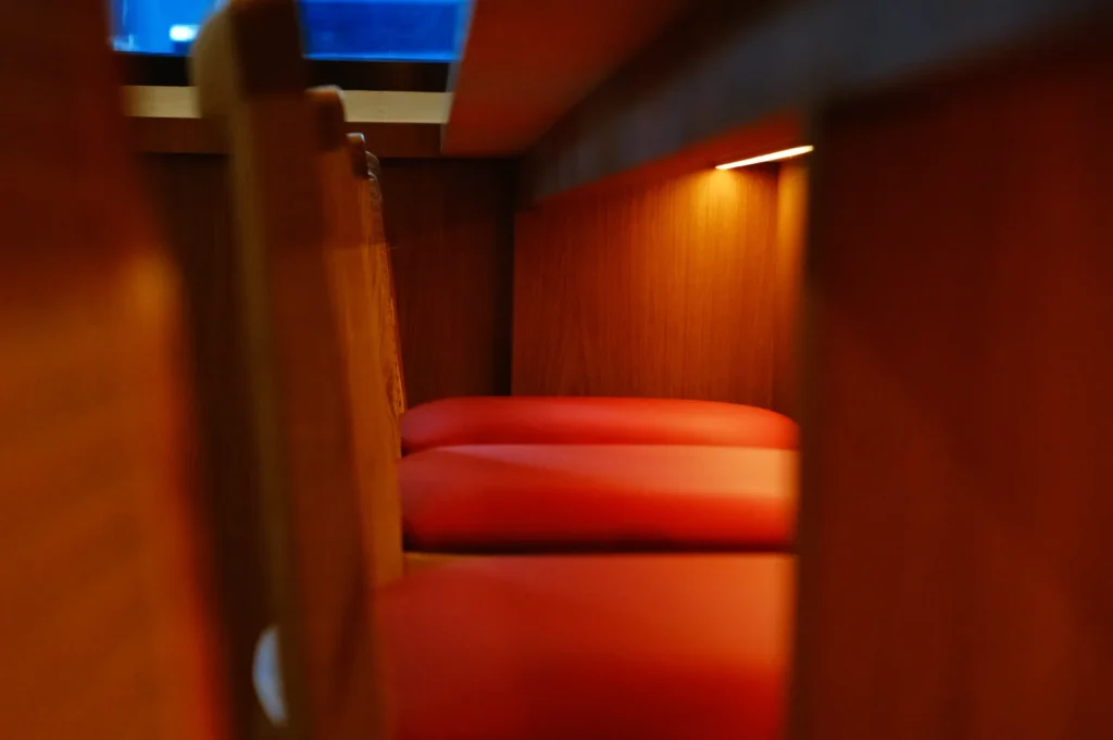 A close-up view of a cozy seating area with red cushions and wooden panels, partially illuminated.