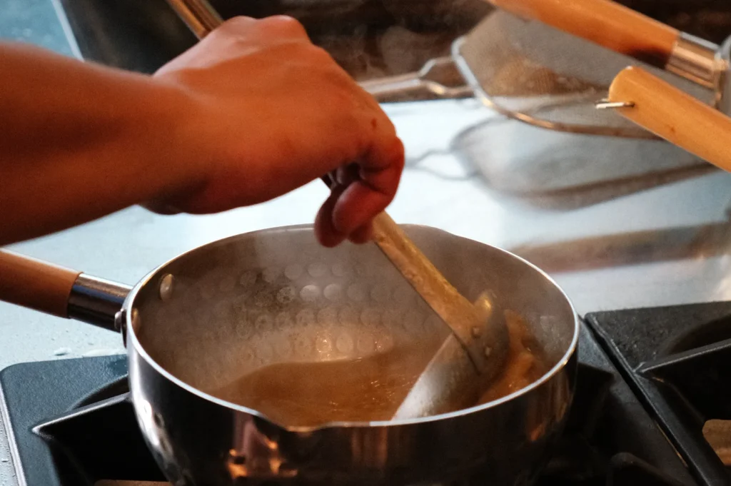 Chef Masa stirring a pot on a stove with steam rising.