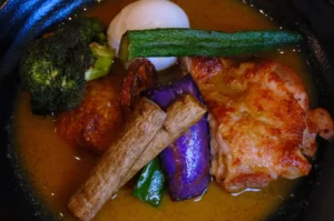 A bowl of curry featuring chicken, broccoli, okra, egg, and various vegetables including eggplant and green chili.