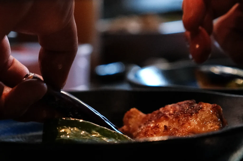 A close-up of hands using a fork to pick up food from a plate in a dimly lit setting.