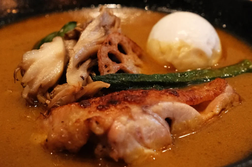 A bowl of soup curry with chicken, mushrooms, a soft-boiled egg, and vegetables in a rich broth.