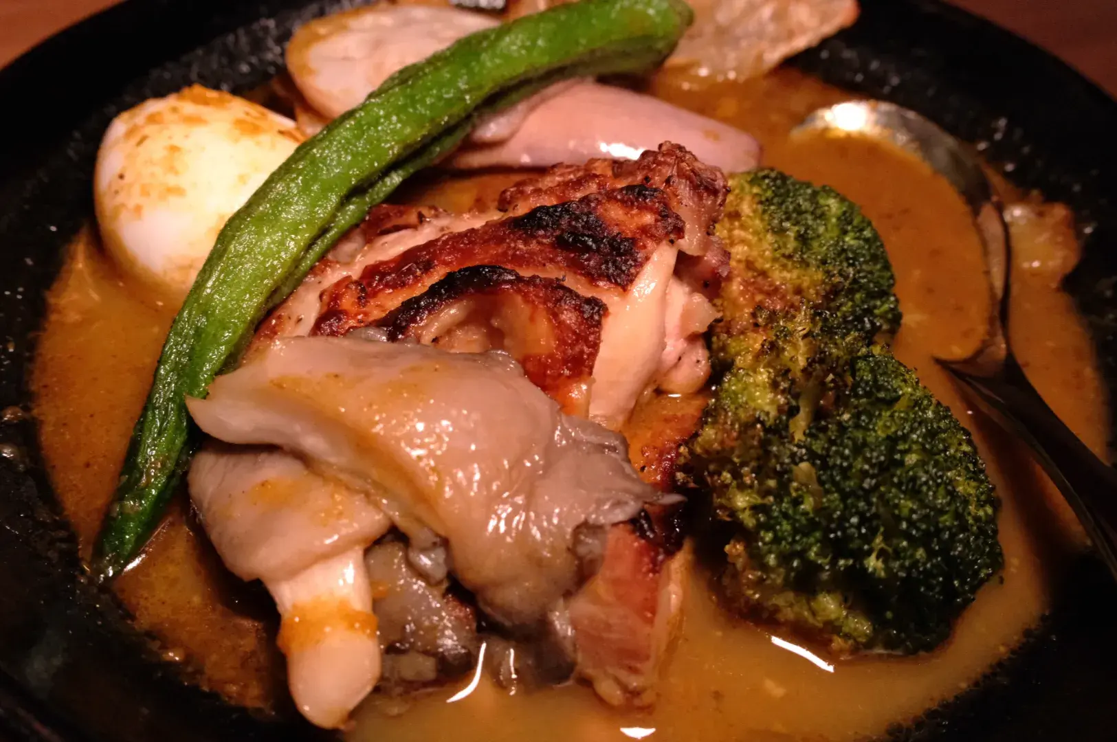 A plate of grilled chicken with vegetables, including broccoli and green beans, served in a rich sauce.