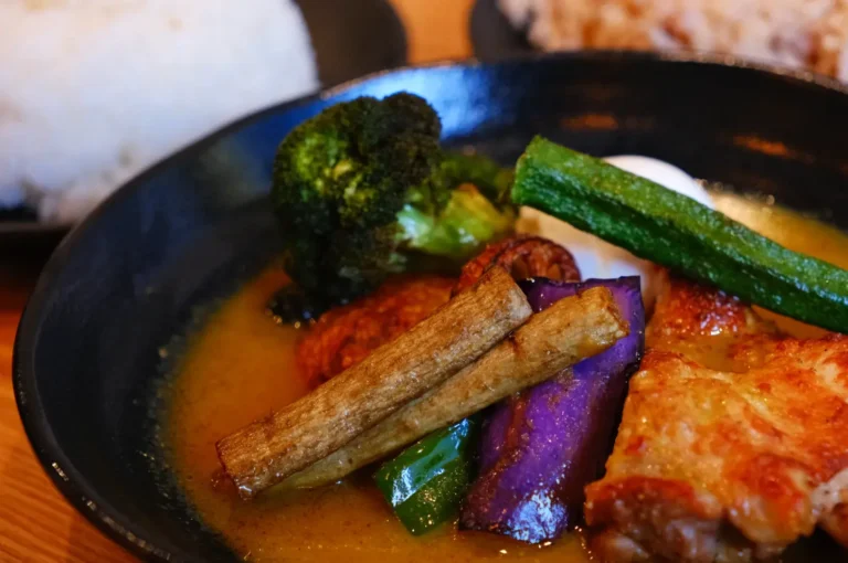 A plate of food featuring various vegetables, including broccoli, okra, and purple eggplant, accompanied by chicken in a saucy broth.
