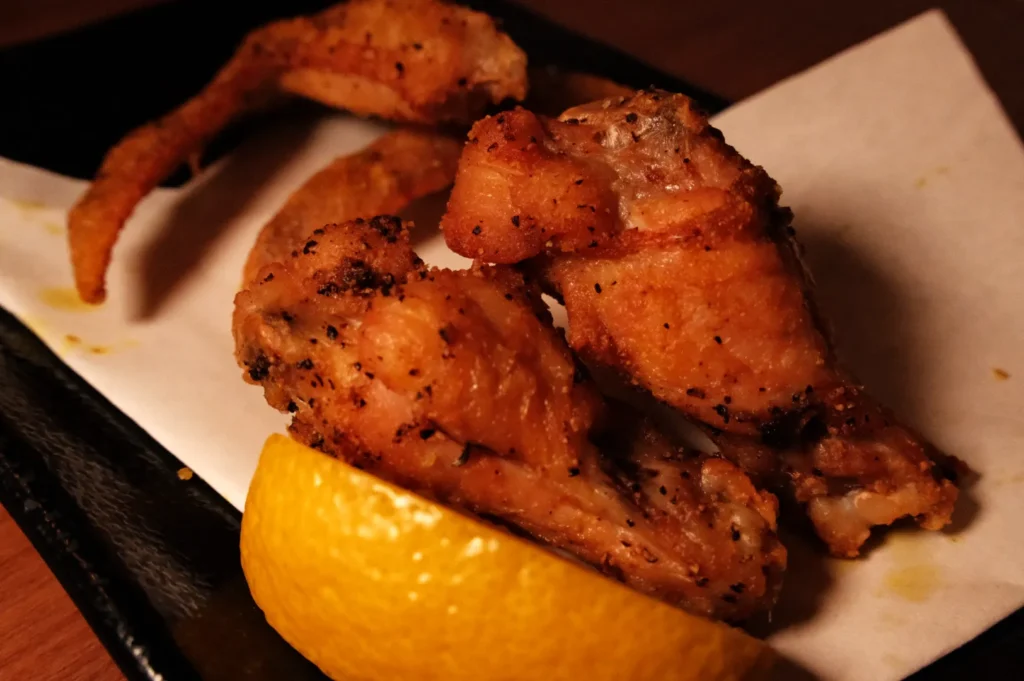 A plate of crispy fried chicken wings served with a slice of lemon.