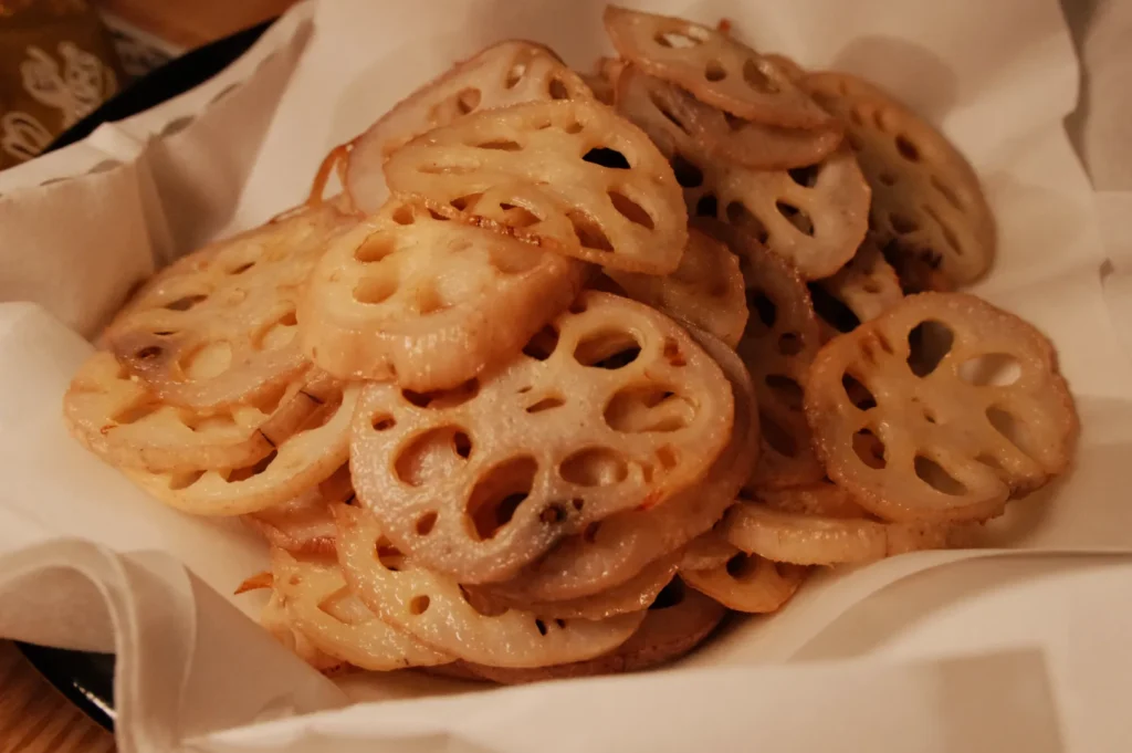 A plate of sliced and cooked lotus root, arranged neatly and served on a white paper lining.