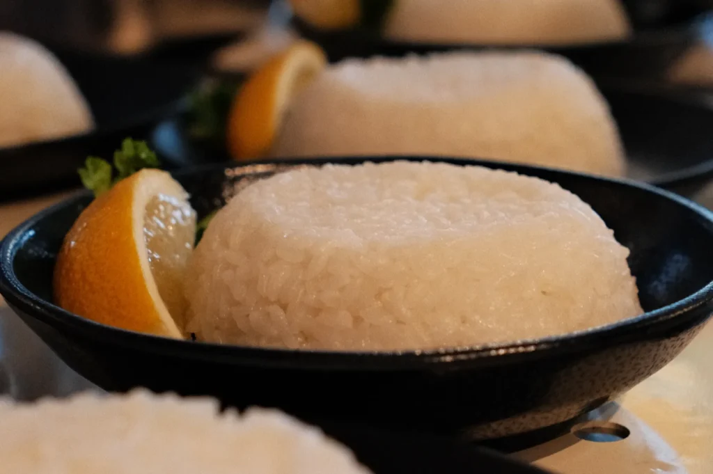 A close-up of a plate of rice shaped into a mound, garnished with a lemon wedge and a sprig of parsley.