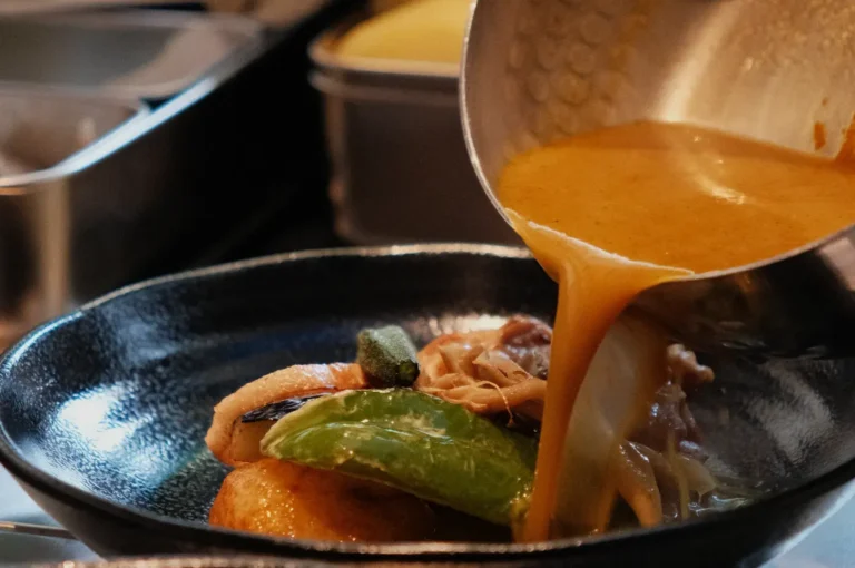 A dish being served with sauce being poured over it, featuring various ingredients like vegetables and meat in a bowl.
