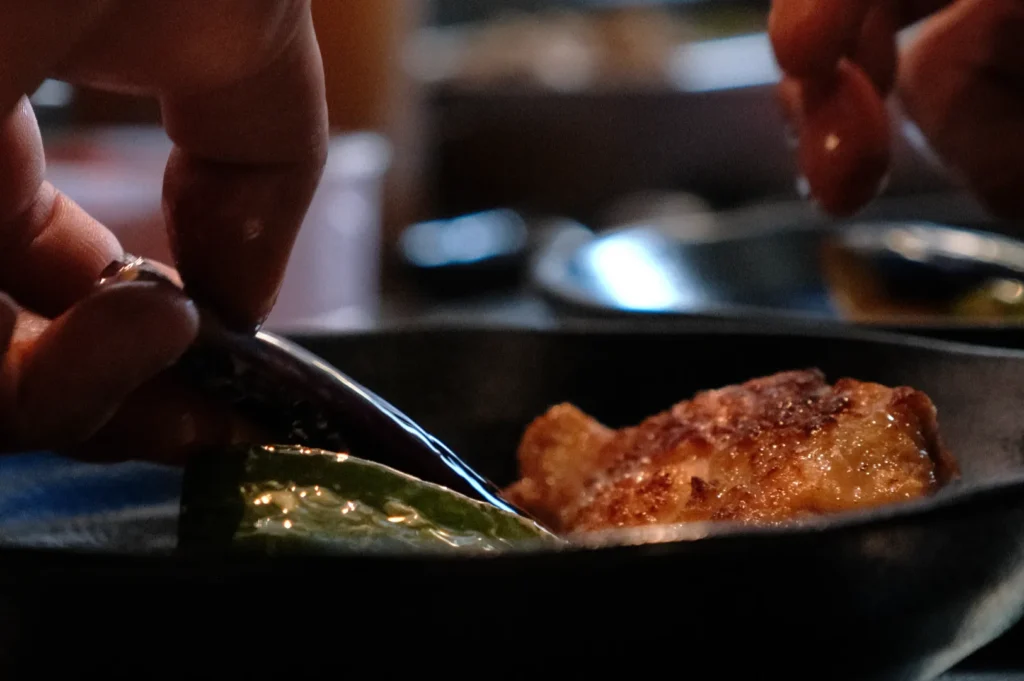 A close-up of a hand using a spoon to serve food from a black dish.