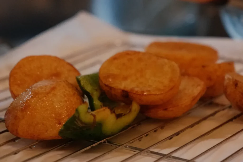 Golden, round fried cakes and a roasted green pepper rest on a wire rack over parchment, creating a warm, rustic close-up of freshly cooked food.