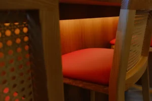 A close-up view of a wooden chair with a red cushion, partially illuminated from below, showing another chair in the background.