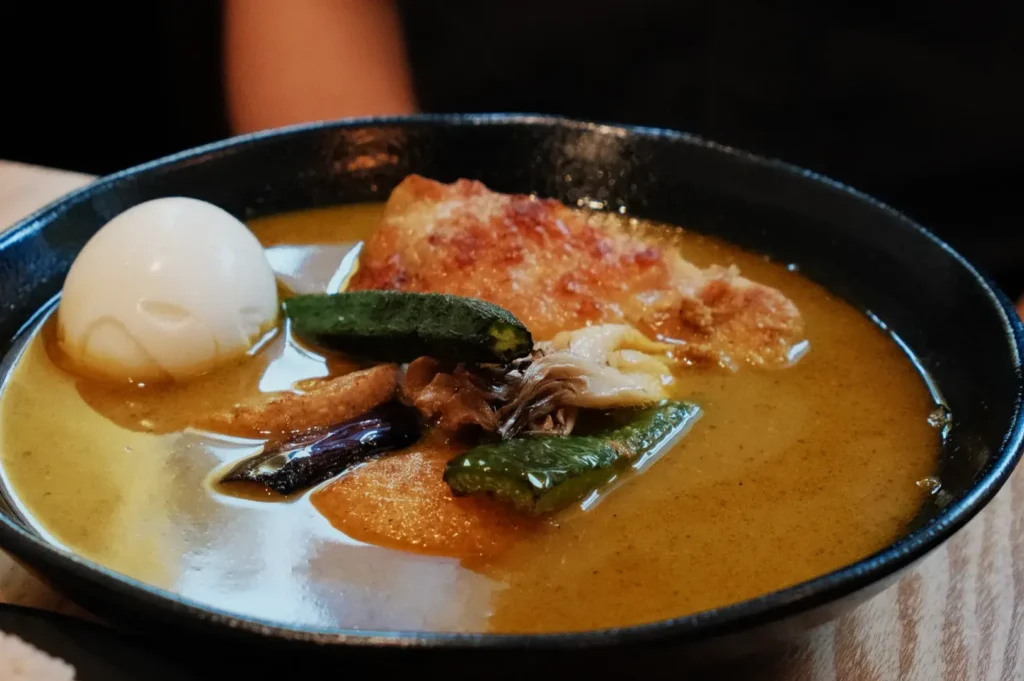 A bowl of curry with a soft-boiled egg, pieces of meat, and various vegetables.