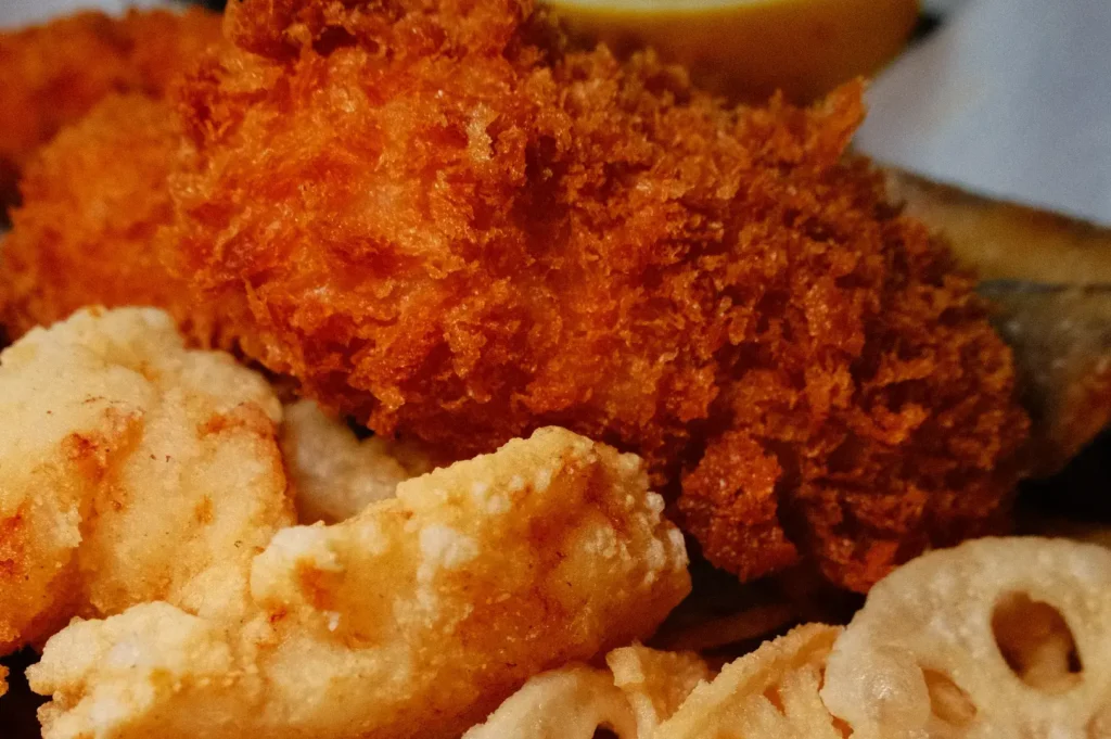 A close-up of golden-brown breaded fried seafood, with crisp orange-coated pieces and pale battered rings on a plate; warm, hearty comfort-food feel.
