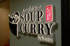 Illuminated restaurant sign reads “Soup Curry” and “By Ki-Setsu,” with Japanese lettering and a bowl illustration; warm, inviting storefront atmosphere.