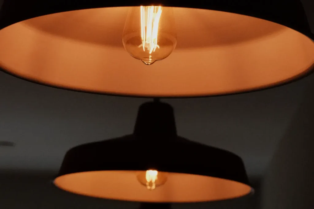 Close-up of a glowing vintage bulb inside a wide black pendant lamp, its warm amber light reflecting below and creating a cozy, intimate mood.