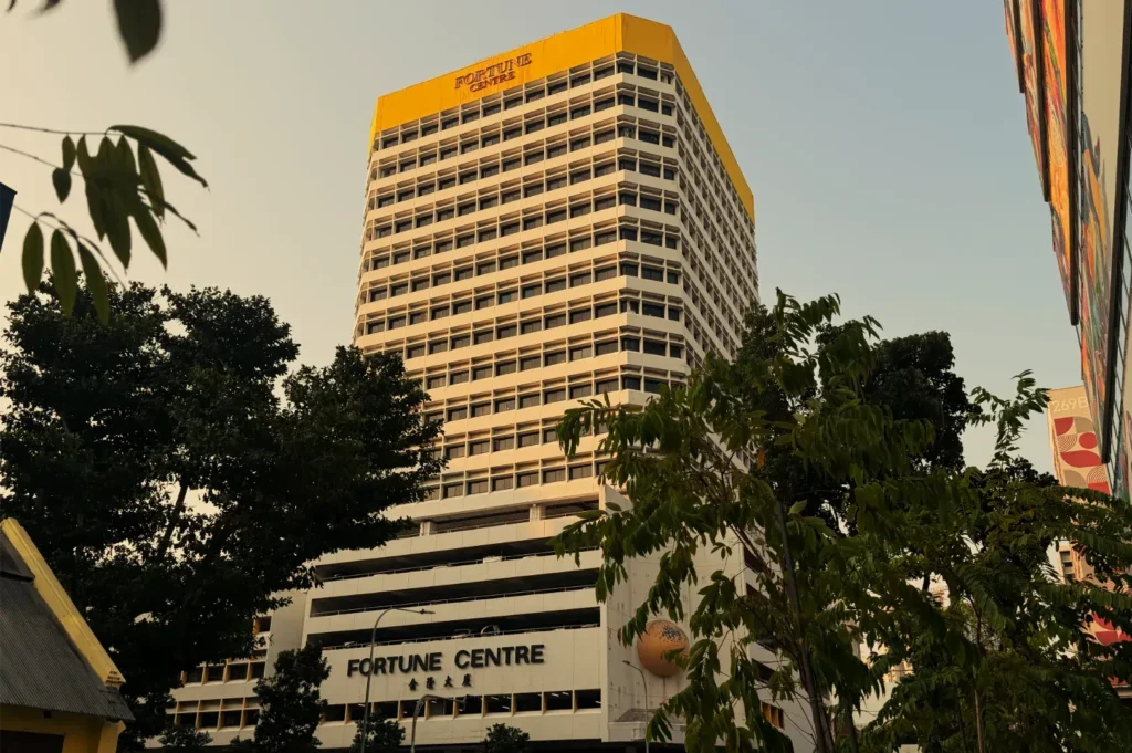 A yellow-and-white Fortune Centre office tower rises above leafy trees in warm evening light, giving the urban streetscape a calm, golden tone.
