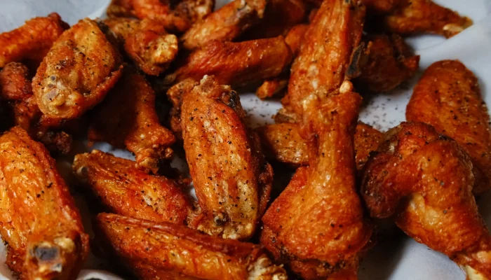 A close-up of golden-brown chicken wings with a crispy texture, arranged on a sheet of parchment paper.