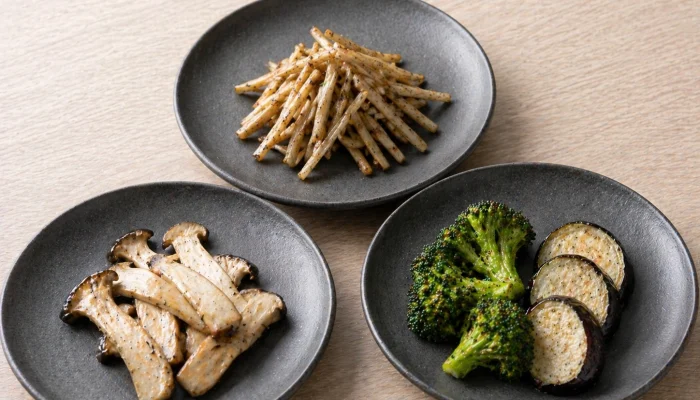 Three small plates featuring grilled broccoli with eggplant, sautéed king oyster mushrooms, and seasoned burdock root.