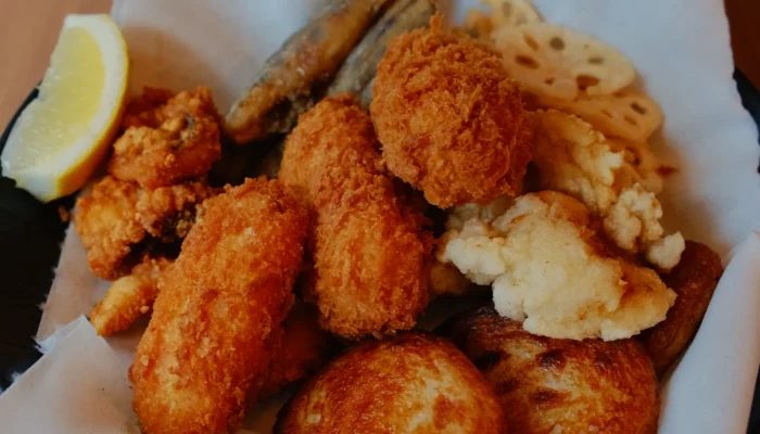 A plate of assorted fried foods, including croquettes, fish, and sliced lotus root, garnished with a lemon wedge.